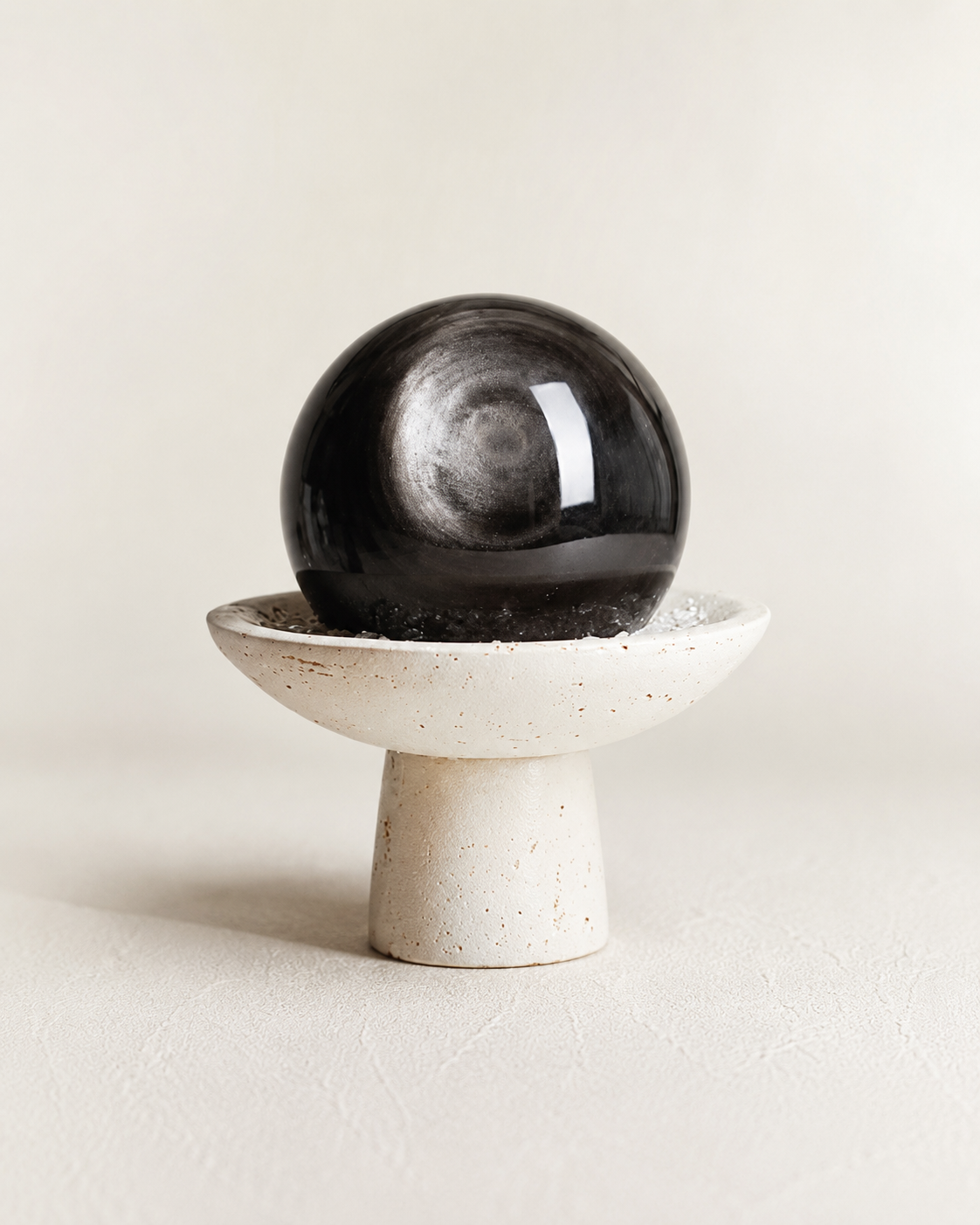 Black crystal sphere displayed on a sculptural ceramic stand